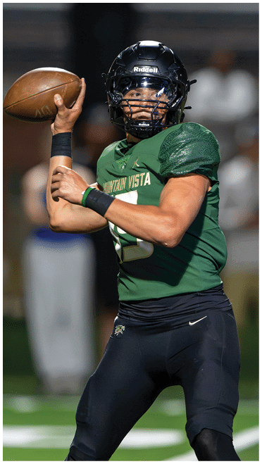 A person wearing a dark sleeve is holding a brown leather football in their hand against a blurred dark background. Description generated by AI
