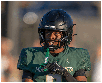 A person wearing a dark football helmet and green jersey looks to the side with a focused expression. Description generated by AI