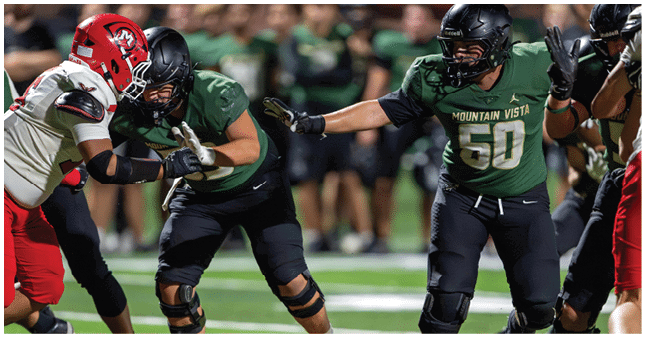 Two people in green football uniforms from Mountain Vista are engaging with an opponent in a white and red uniform on a football field during a game. Description generated by AI