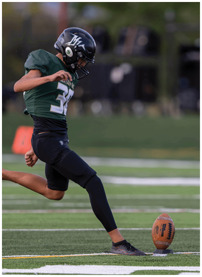 A person wearing a dark helmet and sports uniform is preparing to kick a football on a grassy field. Description generated by AI