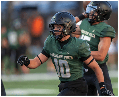 Two people in green football uniforms and helmets are actively playing on a field with one person in the foreground running and the other in the background preparing to throw a football. Description generated by AI