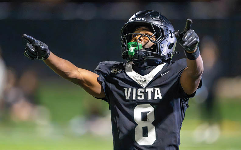 A person wearing a black football uniform with the word VISTA and the number 8 on it is raising their arms in celebration on a field. Description generated by AI