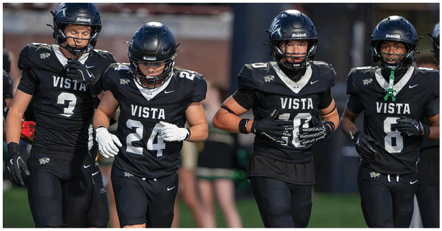 Four people wearing black football uniforms with the word Vista on the front are walking together on a field. Description generated by AI