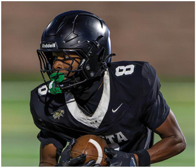 A person wearing a black football uniform and helmet is holding a football while running on a field. Description generated by AI