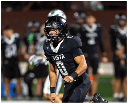 A person wearing a black football uniform with the word Vista and the number 0 is celebrating on a field with blurred players in the background. Description generated by AI