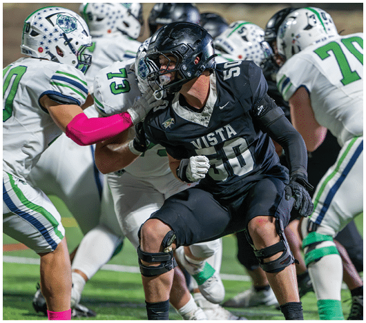 A group of people in football uniforms are engaged in a play on a field with one player in a black uniform being tackled by players in white uniforms. Description generated by AI
