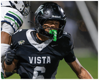 Two people in football uniforms are engaged in a play on a field, with one wearing a black uniform labeled “VISTA" and the other in a white uniform with green and blue stripes. Description generated by AI