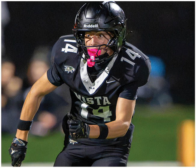 A person wearing a black football uniform with the number 14 and a helmet is running on a field during a game. Description generated by AI