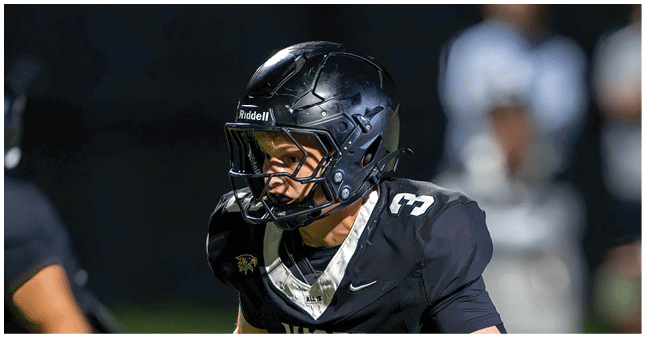 A person wearing a black football helmet and black jersey with the number 3 is focused and appears to be in action during a nighttime football game. Description generated by AI