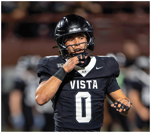 A person wearing a black football uniform with the word VISTA and the number 0 is adjusting their helmet on a blurred sports field. Description generated by AI