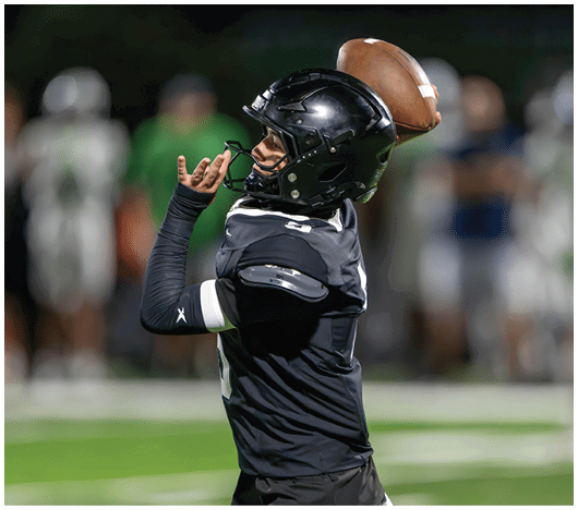A person wearing a black football helmet and uniform is preparing to throw a football during a game. Description generated by AI