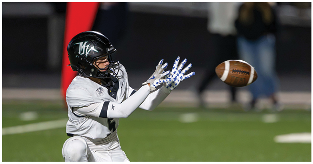 A person wearing a football helmet and gloves is reaching out to catch a football on a field. Description generated by AI