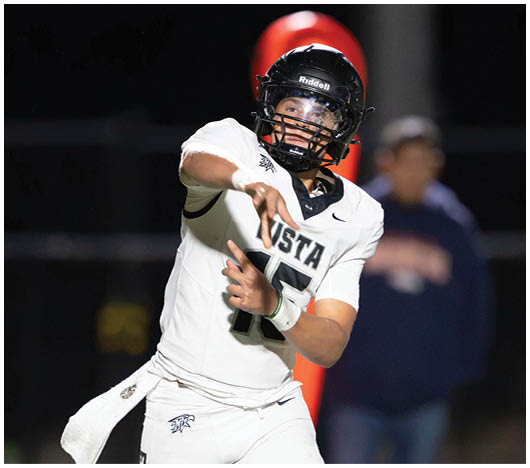 A person wearing a white football uniform and helmet is throwing a football during a nighttime game. Description generated by AI
