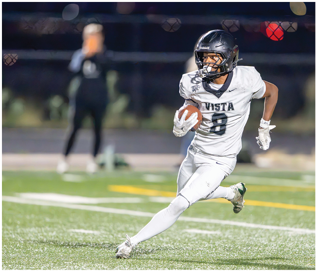 A person in a white football uniform with the word Vista and the number 8 is running on a field while holding a football. Description generated by AI