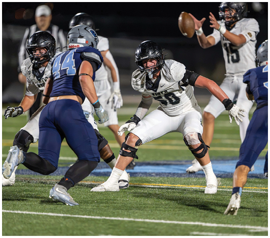 People in football uniforms are actively engaged in a play on a well-lit field during a nighttime game. Description generated by AI