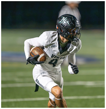 A person wearing a white football uniform and black helmet is running on a field while holding a football. Description generated by AI