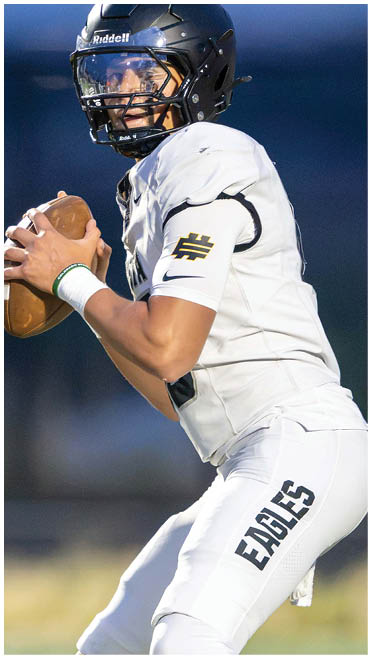 A person wearing a white football uniform with “EAGLES" on the pants and a black helmet is holding a football in a ready-to-throw position. Description generated by AI