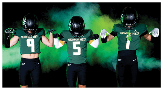 Three people wearing Mountain Vista football uniforms and helmets stand side by side against a smoky green and yellow background with their arms flexed to show strength. Description generated by AI