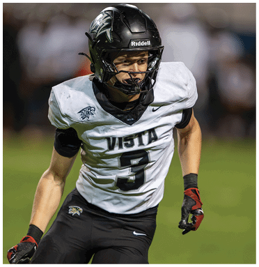 A person wearing a black helmet and white football jersey with the number 3 and the word Vista is running on a grassy field. Description generated by AI