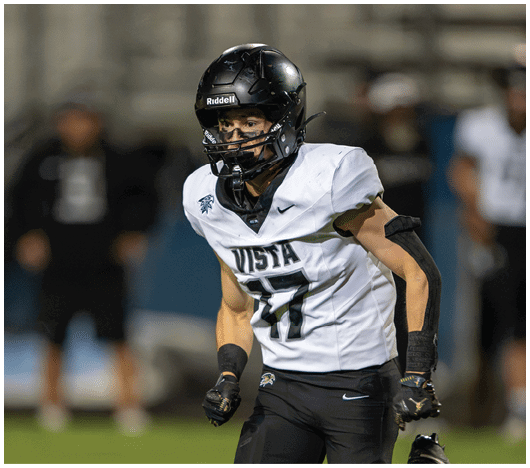 A person wearing a black helmet and white football jersey with the word Vista and number 17 is on a football field during a game. Description generated by AI