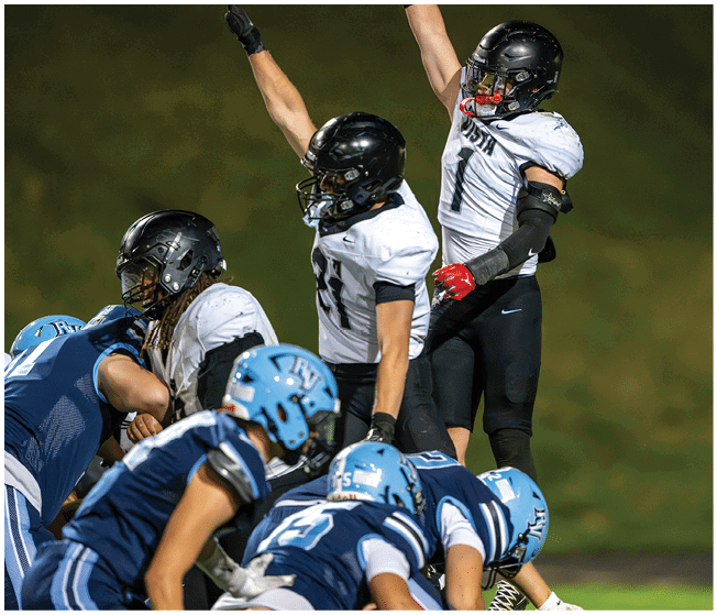 A group of football players in black and white uniforms celebrate on the field while opposing players in blue uniforms prepare for the next play. Description generated by AI