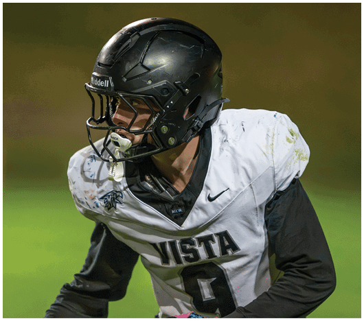 A person wearing a black helmet and a white football jersey with the word Vista and the number 9 is actively engaged in a football game. Description generated by AI