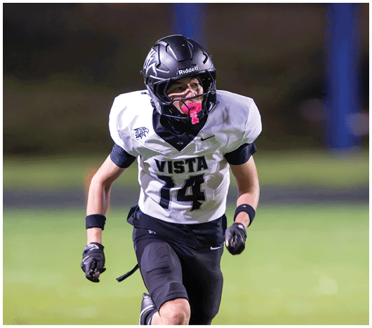 A person wearing a football uniform with the number 14 and a helmet is running on a field with a focused expression. Description generated by AI