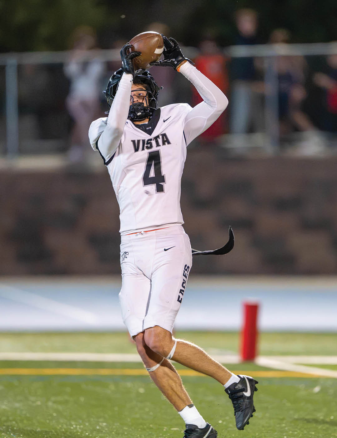 A person wearing a white football uniform with the number 4 and the word Vista is jumping to catch a football on a field. Description generated by AI