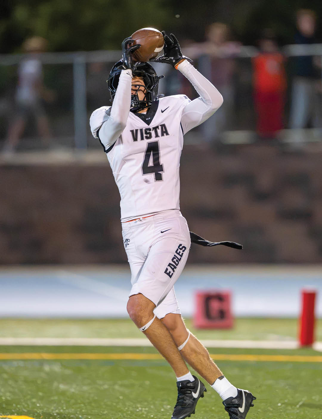 A person wearing a white football uniform with the word Vista and number 4 is jumping to catch a football on a field. Description generated by AI