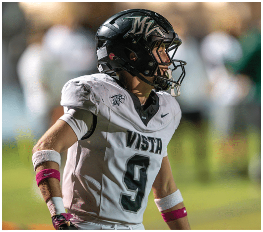 A person wearing a black football helmet and a white jersey with the number 9 and the word Vista stands on a field with hands on hips. Description generated by AI