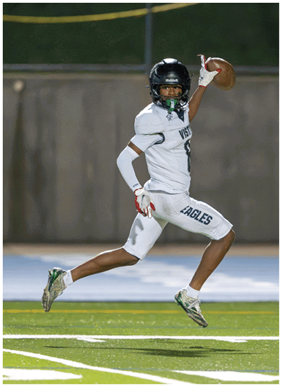 A person in a white football uniform with “EAGLES" on the pants is running on a field while holding a football in one hand. Description generated by AI