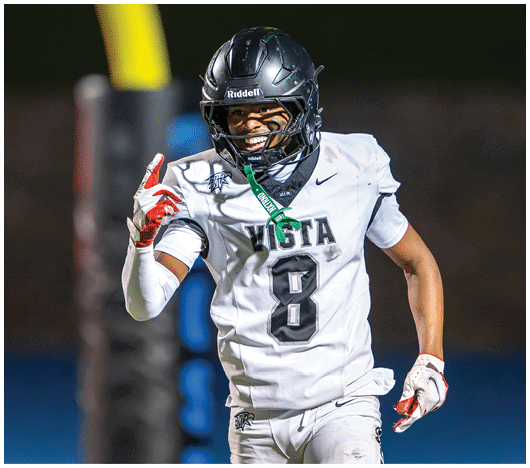 A person wearing a white football uniform with the number 8 and a black helmet is celebrating on the field with a smile and one finger raised. Description generated by AI