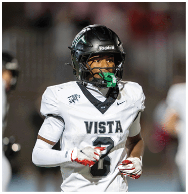 A person wearing a white football uniform with the word Vista and the number 8 on it is standing on a field with a black helmet and a green mouthguard. Description generated by AI