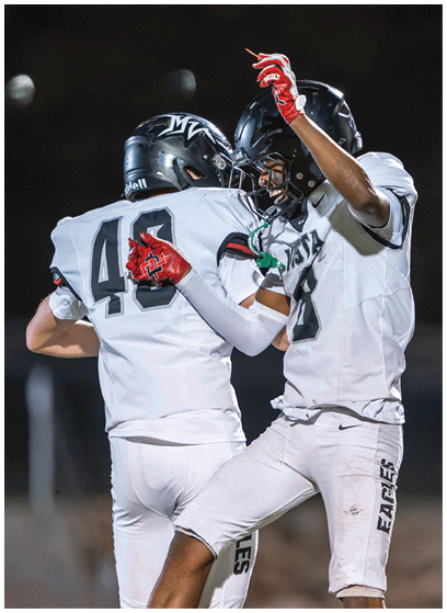 Two people wearing football helmets and uniforms are celebrating with one person smiling and the other showing the number 40 on their jersey. Description generated by AI
