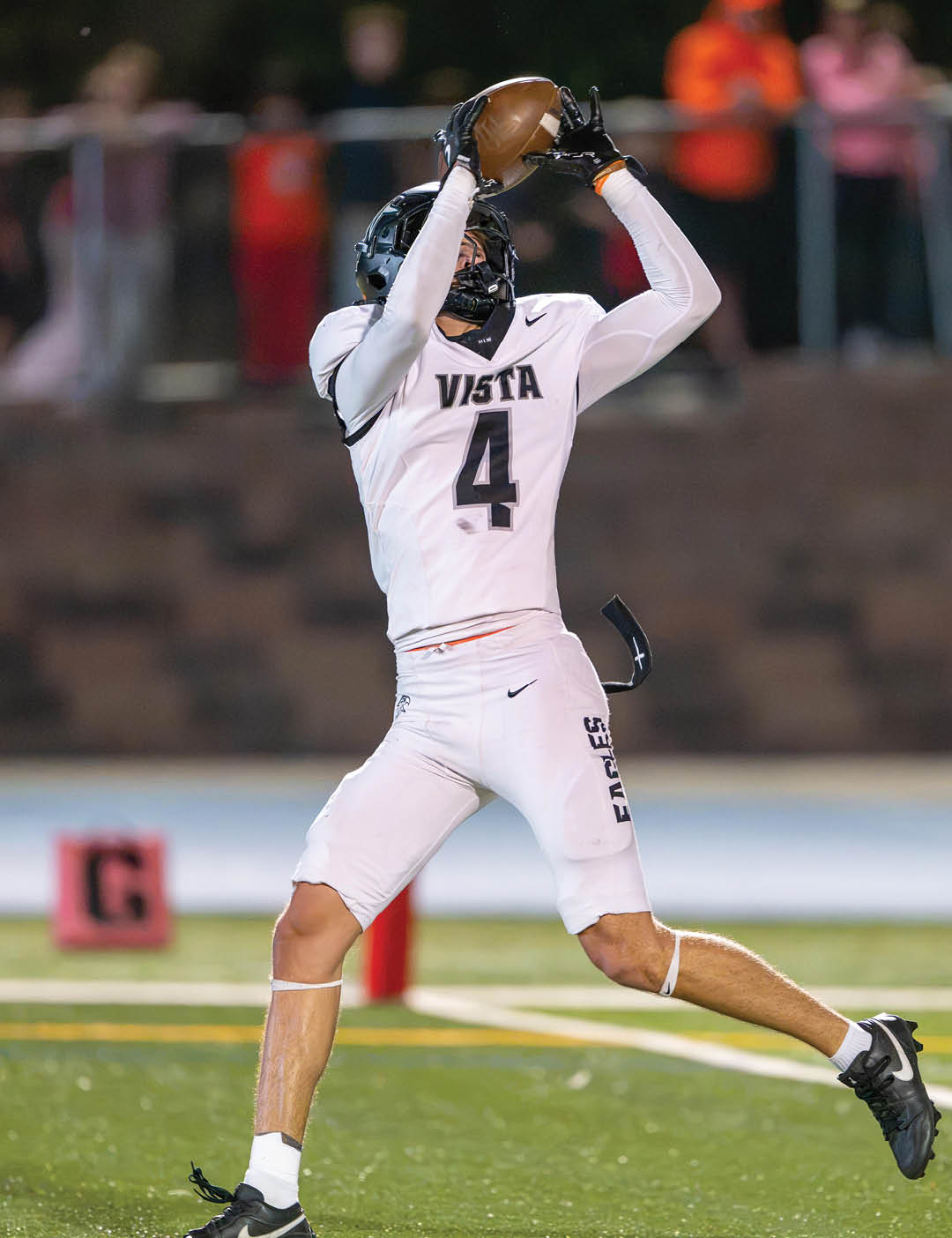 A person wearing a white football uniform with the number 4 and the word Vista is catching a football on a field during a game. Description generated by AI