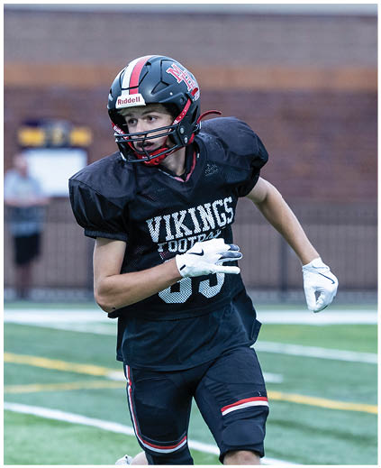 A football player wearing a black jersey with the word Vikings on it. Description generated by AI