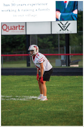 A football player in a white jersey and red shorts is crouching on the field. Description generated by AI