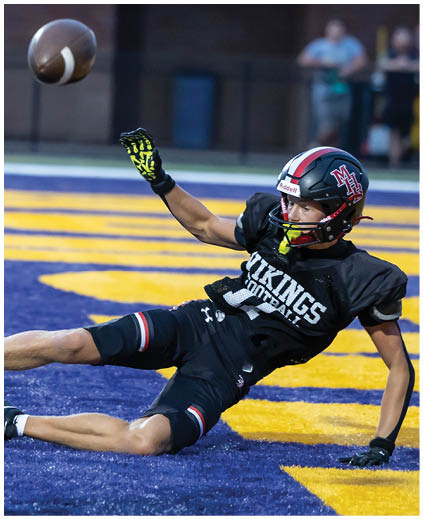A football player in a black jersey with the number 12 on it is diving for a football. Description generated by AI