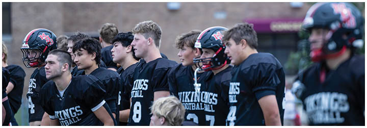 A group of football players wearing black jerseys with the word Vikings on the front. Description generated by AI
