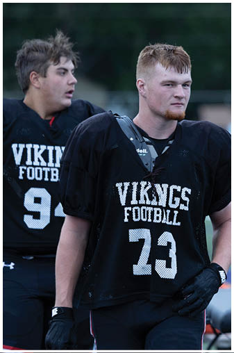 Two football players wearing black jerseys with the word Vikings on them. Description generated by AI