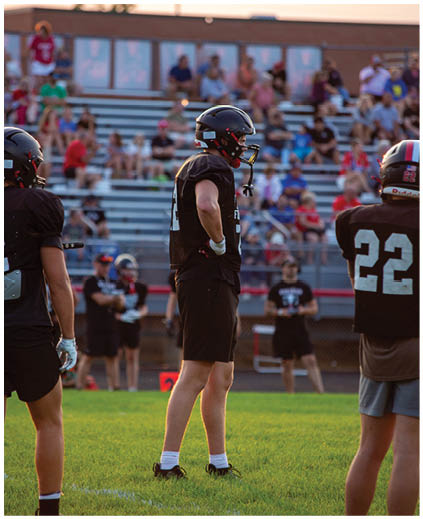A football player in a black jersey stands on a field. Description generated by AI