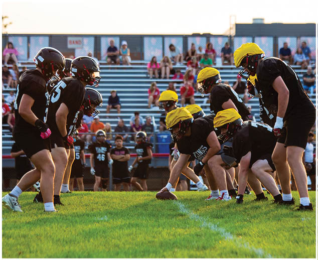 A group of football players in black and yellow uniforms are on a field. Description generated by AI
