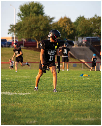 A person wearing a black shirt and black helmet is standing in a grassy field. Description generated by AI