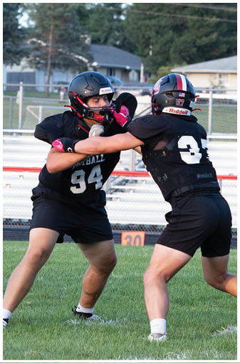 Two football players in black uniforms on a field. Description generated by AI