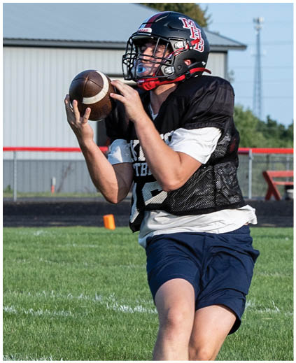 A football player in a black and white uniform holding a football. Description generated by AI