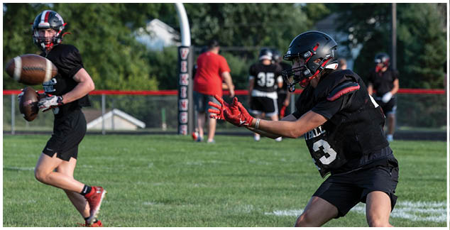 A football player in a black jersey with the number 3 on it catching a football. Description generated by AI