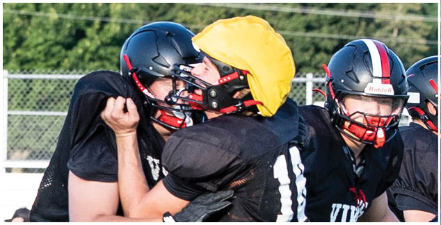 A football player in a black jersey is tackled by another player. Description generated by AI