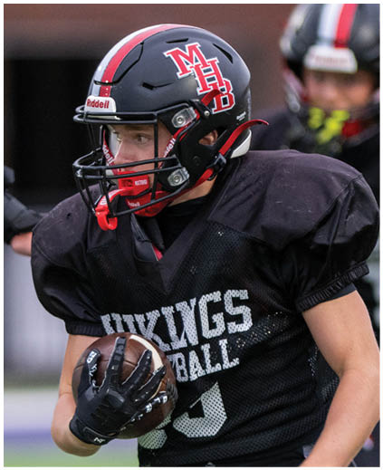 A boy in a green jersey is running with a football. Description generated by AI