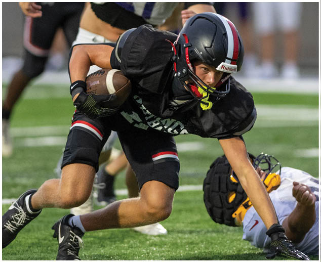 A football player in a black jersey is running with a football. Description generated by AI