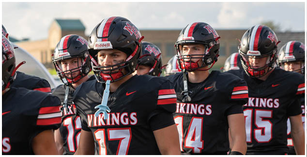 A group of football players wearing black jerseys with the word Vikings on them. Description generated by AI
